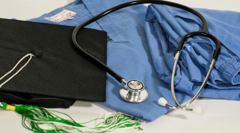 graduation cap next to scrubs and stethoscope
